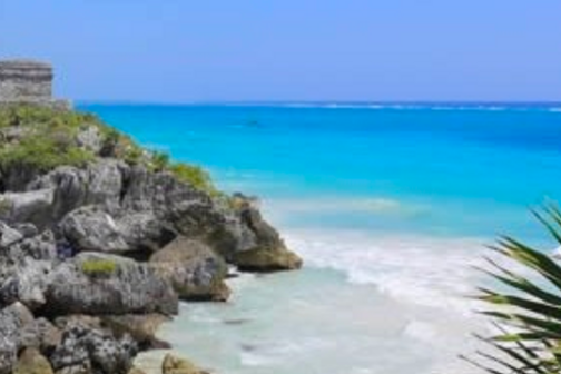 a rocky beach next to the ocean with Tulum in the background